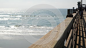 Wooden pier waterfront boardwalk, California beach USA. Defocused ocean, sea waves. People walking.