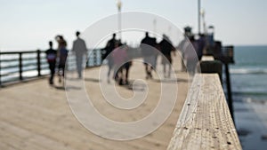 Wooden pier waterfront boardwalk, California beach USA. Defocused ocean, sea waves. People walking.