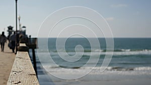 Wooden pier waterfront boardwalk, California beach USA. Defocused ocean, sea waves. People walking.