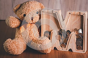 Wooden piggy bank with brown teddy bear. Money saving concept. Vintage picture style