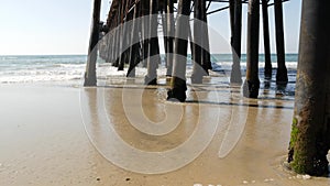 Wooden piles under pier in California USA. Pilings, pylons or pillars below bridge. Ocean waves tide
