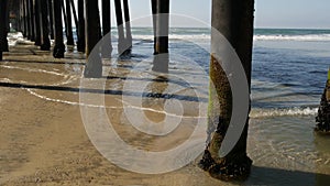 Wooden piles under pier in California USA. Pilings, pylons or pillars below bridge. Ocean waves tide