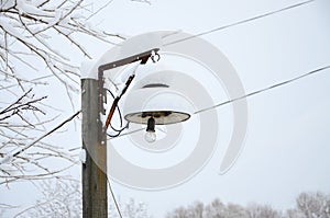 A wooden pillar with a hanging lamp. The plafond of the lamp is covered with a thick layer of snow