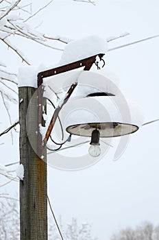 A wooden pillar with a hanging lamp. The plafond of the lamp is covered with a thick layer of snow