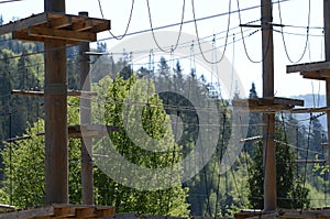 Wooden pillars and hanging ropes of a rope park on the background of green forest in the Carpathians. Ukraine