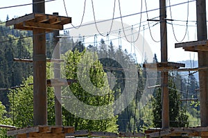 Wooden pillars and hanging ropes of a rope park on the background of green forest in the Carpathians. Ukraine