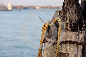 Wooden pillars with old rope and chain in sea at Venice dock.