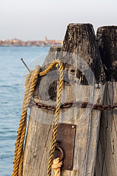 Wooden pillars with old rope and chain in sea at Venice dock.