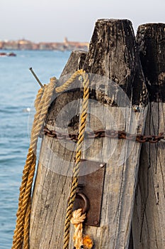 Wooden pillars with old rope and chain in sea at Venice dock.