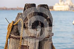 Wooden pillars with old rope and chain in sea at Venice dock.