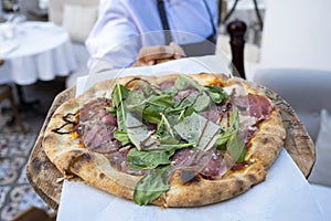 Wooden pizza plate in chef`s hands and meat pizza