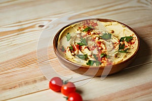 A wooden plate of fresh hummus made of chickpeas, red cherry tomatoes on a blurred wooden background.