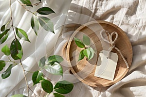 Wooden plate with blank label and green leaves on a beige fabric background