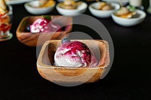 Wooden plate of blueberry ice cream with fresh berries on black table.