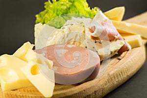 wooden plate with cheeses and cold cuts like gruyere, mortadella, Roquefort and prosciutto