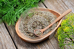 Wooden plate of fennel seeds and bunches of fresh green dill