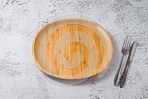 Wooden plate, fork and knife on white stone background. handmade kitchen utensils