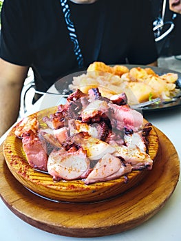 Wooden plate of galician style cooked octopus with potatoes, paprika and olive oil. Pulpo a la gallega