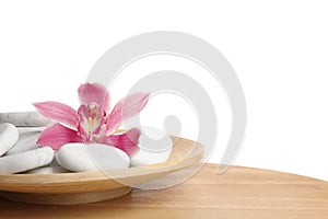 Wooden plate with orchid flower and spa rocks on table against white background.