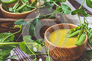 Wooden plate of pea soup and pods of fresh green peas on dark wooden surface