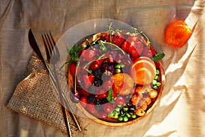 Wooden plate with seasonal fruits and berries background under hard shadows. Strawberries, apricots, cherry, raspberry
