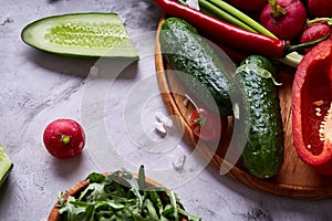 Wooden plate with vegetables for a vegetarian salad on white textured background, close-up, selective focus