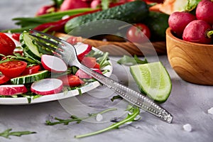 Wooden plate with vegetables for a vegetarian salad on white textured background, close-up, selective focus