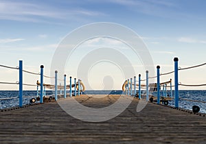 Wooden platform with blue posts with ropes and orange lifebuoys on the background of the sea and sky with clouds Egypt Dahab South