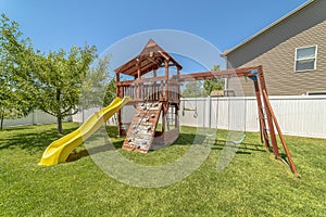 Wooden playground structure with yellow plastic slide swings and climbing wall