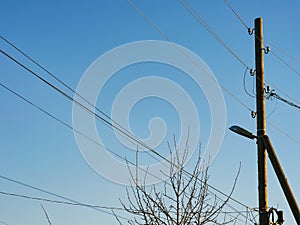 A wooden pole with electric lines and a lamp against blue sky