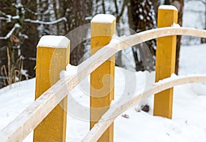 Wooden pole handrail bent beige fence winter road in the forest. yellow bars snow cap