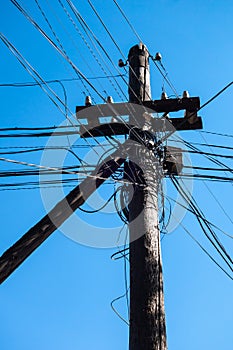 Wooden pole with a transformer, conductors and various cables against a blue sky. photo