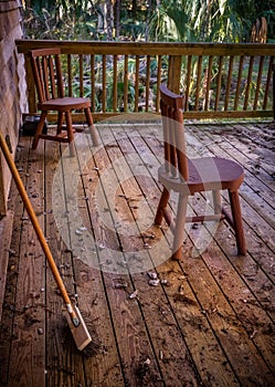 Wooden porch with broom and chairs, littered with debris