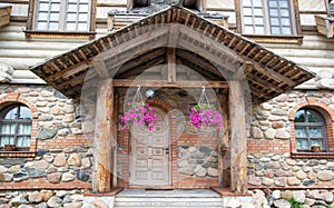 Wooden porch with massive shutters and hanging flowerpots under the roof in a stone building