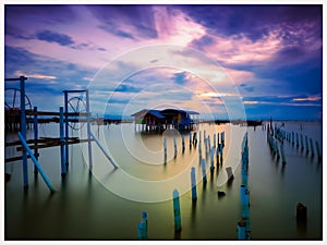 wooden posts in sea against sky during sunset