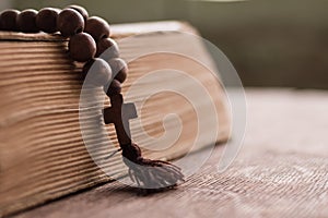 Wooden prayer beads with a Christian cross lie on the holy bible book on a wooden background.