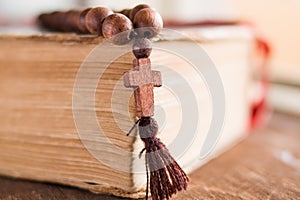 Wooden prayer beads with a Christian cross lie on the holy bible book on a wooden background.