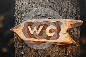 Wooden public toilet sign pointer attached to a tree. WC direction indicator