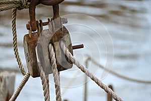 Wooden pulley block with weathered ropes on an historic sailing boat against the blurry sea water