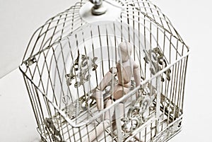 Wooden puppet in bird cage sitting sad