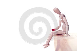 Wooden puppet with small heart sitting on table against white background. Cheating concept