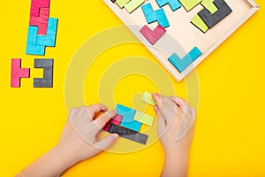 Wooden puzzle and kids hands on yellow background. Flat lay