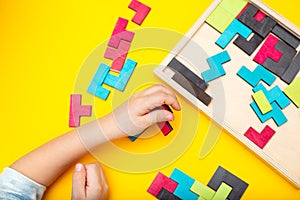 Wooden puzzle and kids hands on yellow background. Flat lay