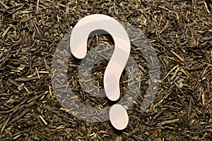 Wooden question mark on green tea leaves. Flat lay. Top view.