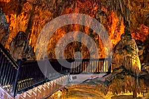 Wooden railing of a staircase against the background of orange-yellow fiery stone formations underground in Damlatas cave Alanya