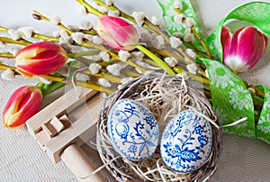 Wooden ratchet instrument with painted blue eggs in wicker nest with pussycats and tulips flower. photo