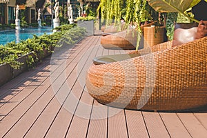 Wooden rattan weave brown chairs with pillow place on terrace beside swimming pool.
