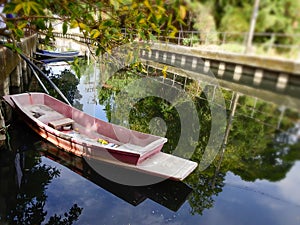Wooden red boat in small csbsl with reflection of tree in clear water