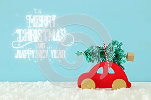 Wooden red car carrying a christmas tree in front of blue background.