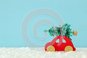 Wooden red car carrying a christmas tree in front of blue background.